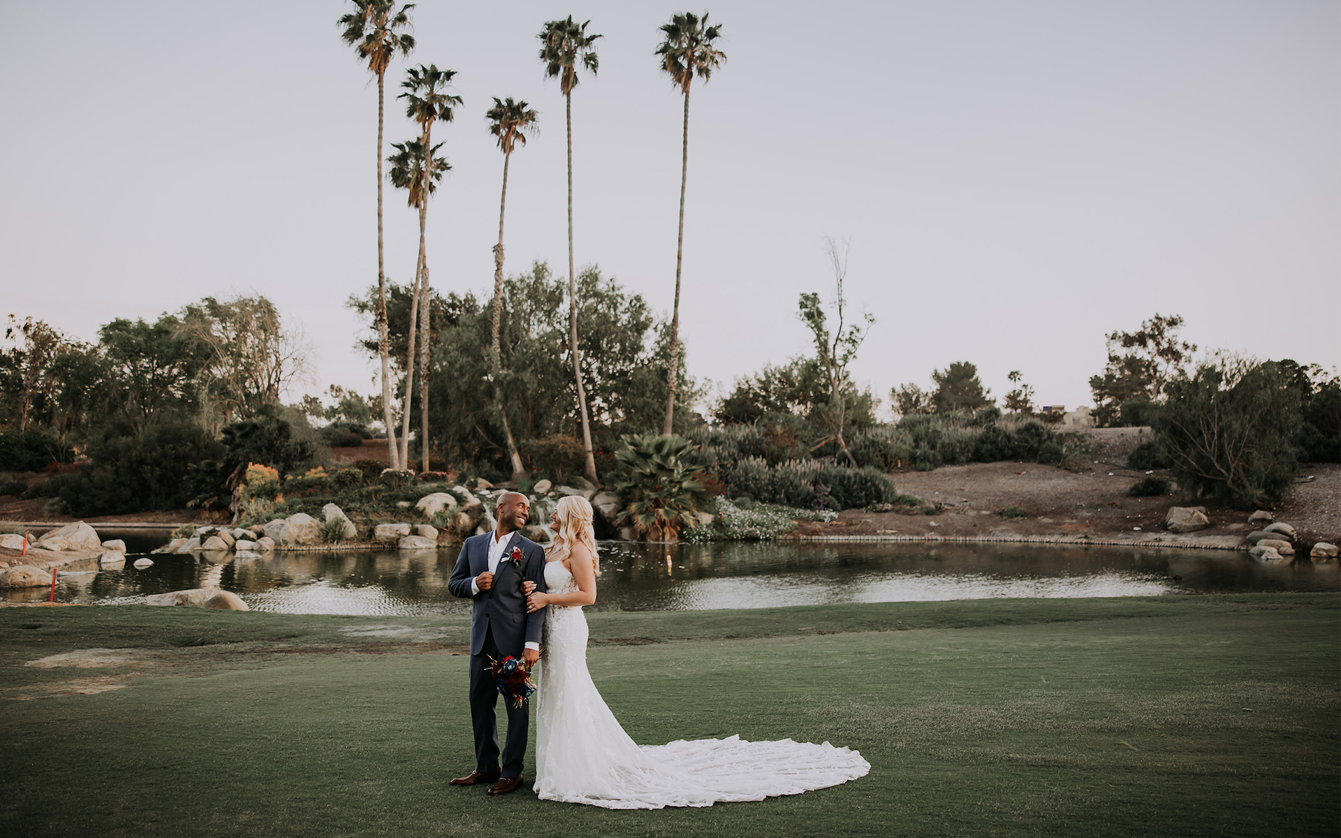 An interracial couple standing on a golf course taking photos on their wedding day 